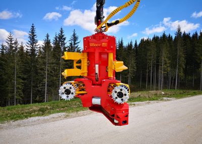 Stroj na ťažbu dreva na lesnej ceste, vybavený reťazami a mechanizmami na spracovanie dreva.